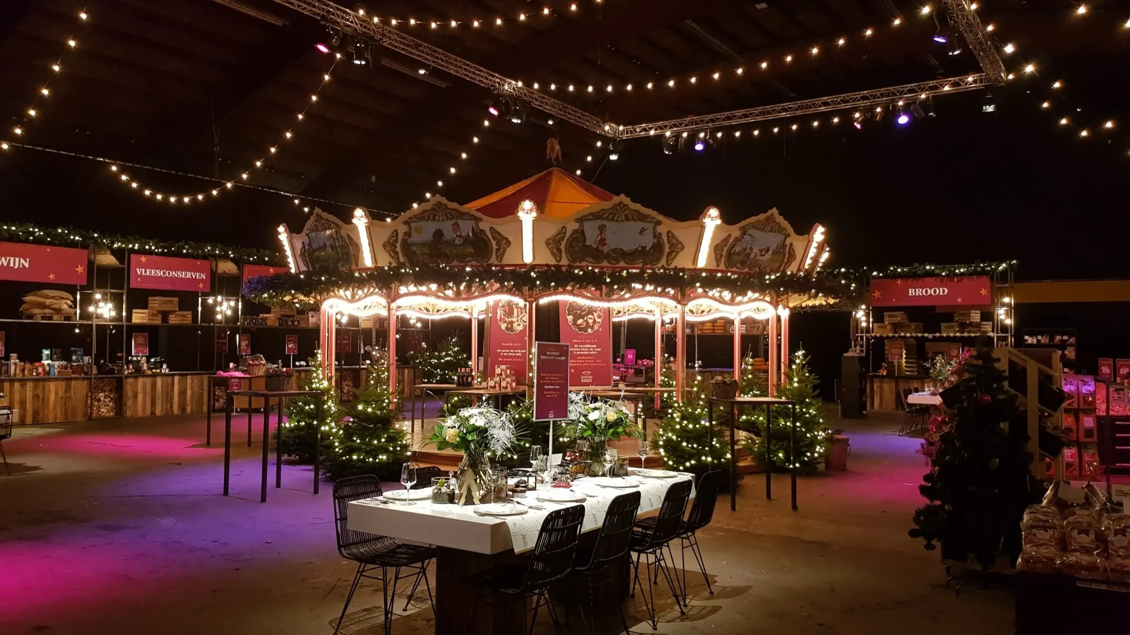 Kerstmarkt in een hal met verlichte draaimolen, kerstbomen en lichtsnoeren