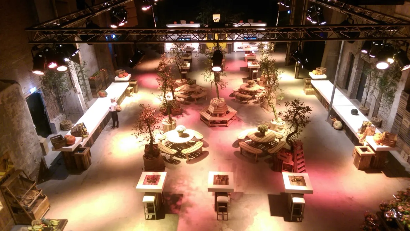 Industriële hal met picknicktafels, olijfbomen en roze licht, van bovenaf