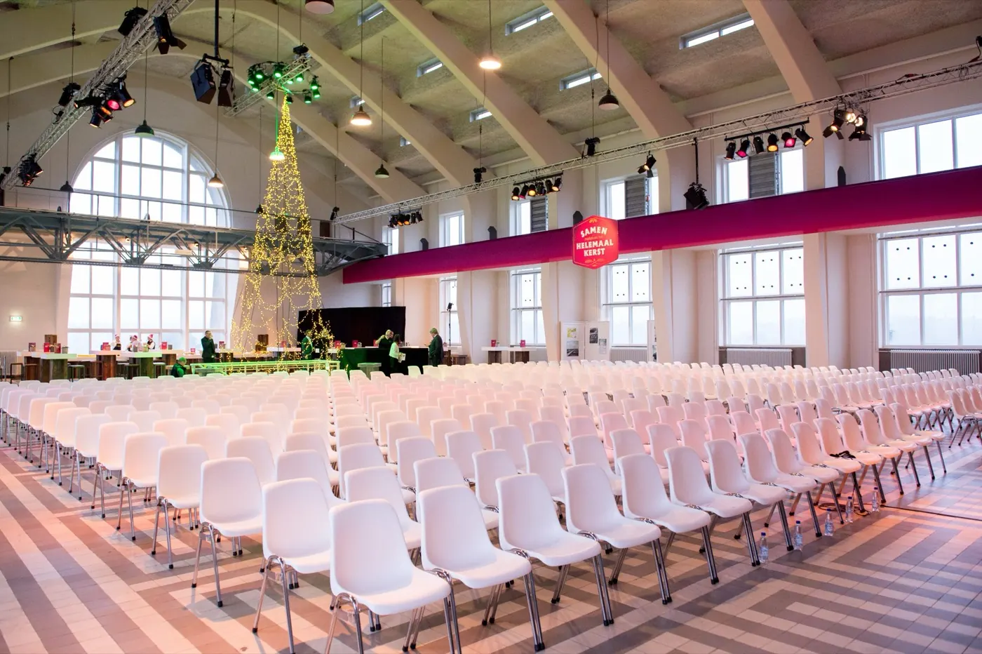 Monumentale zaal met rijen witte stoelen en een verlichte kerstboom